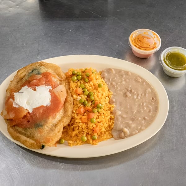 Chili relleno with rice, beans, and two small containers of salsa on a white plate.