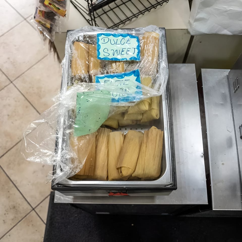A metal tray filled with tamales, some labeled "Dulce Sweet," covered in plastic wrap.